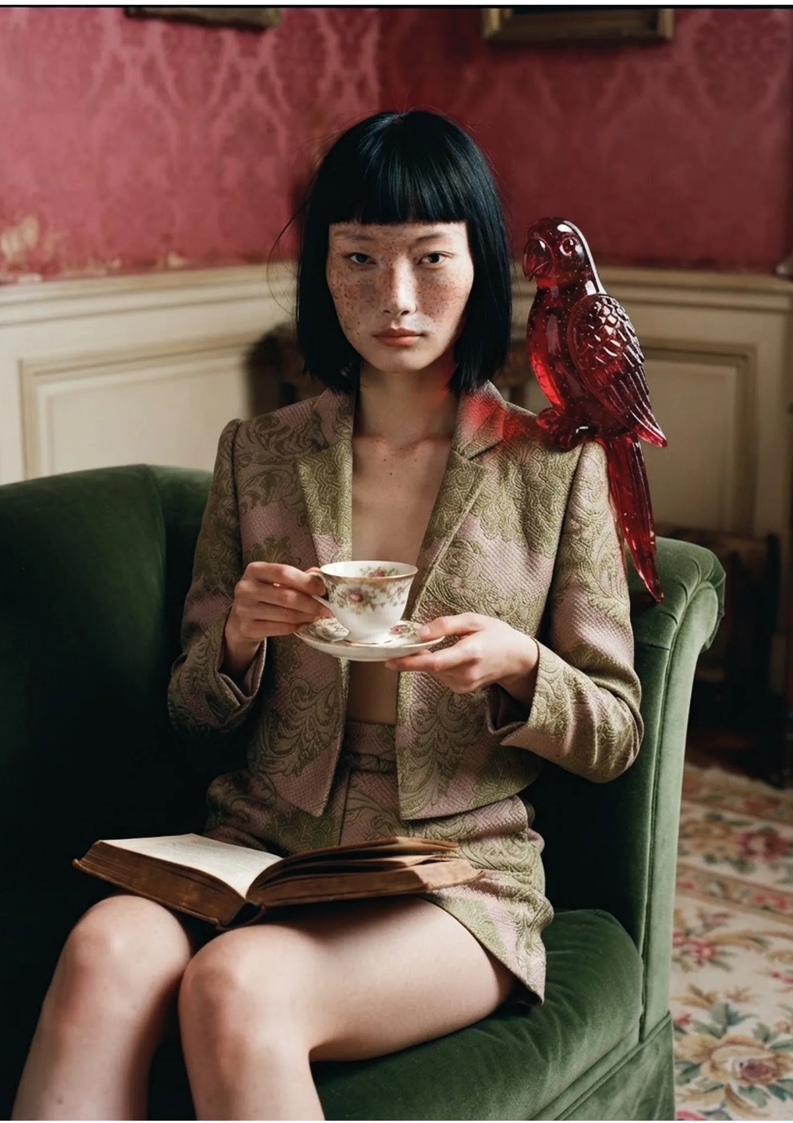 Aylin wearing the same olive brocade blazer, holding a teacup