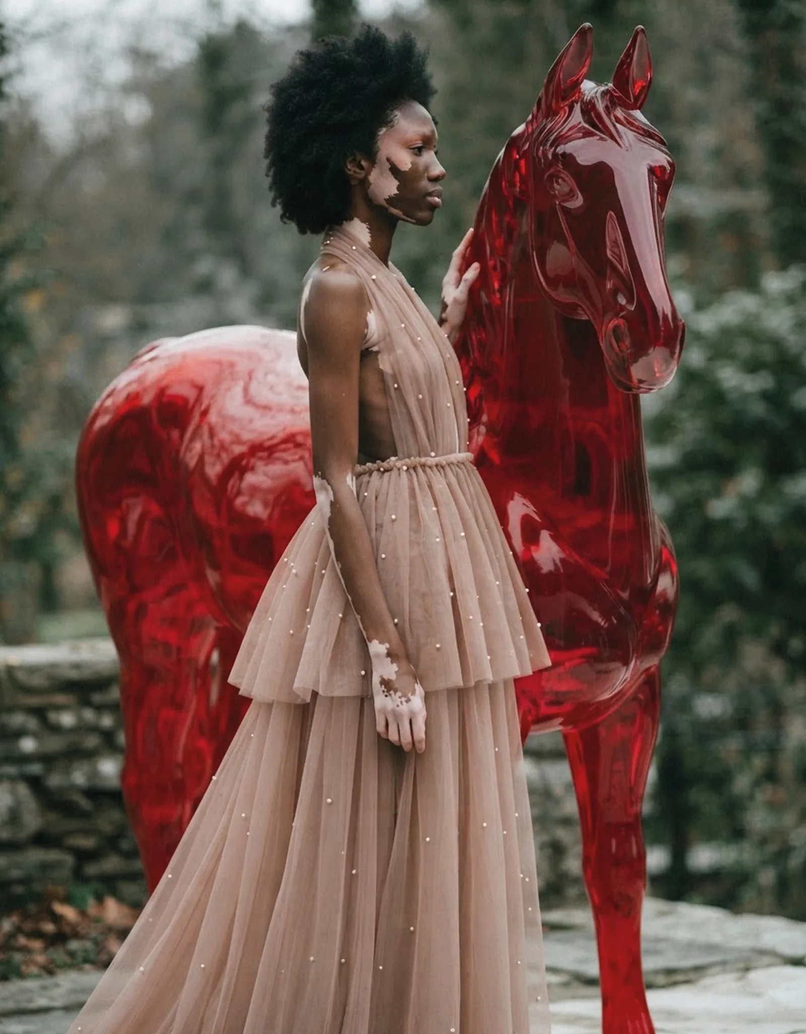 Naima wearing the same tulle dress beside a glass horse