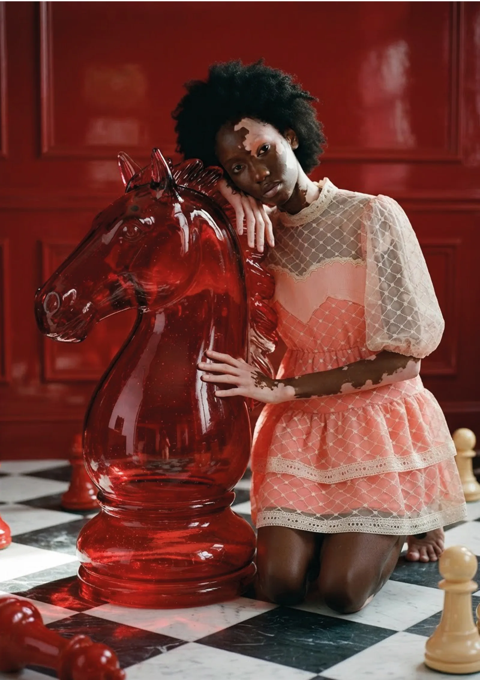 Naima kneeling beside a red glass horse on a chequerboard floor