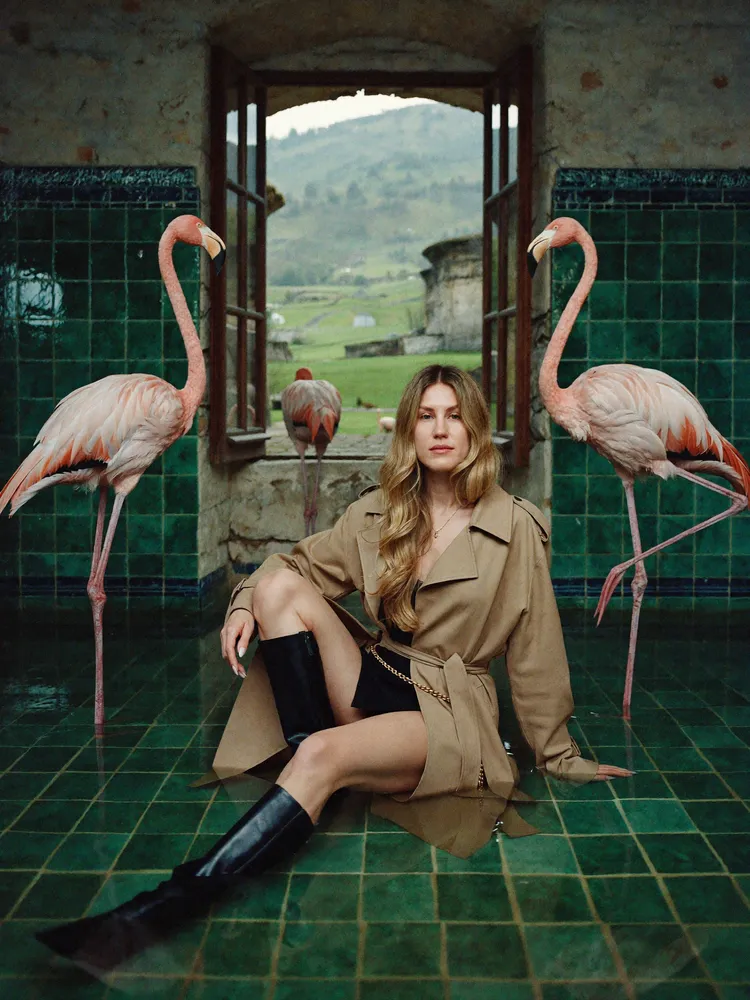 Woman in trench coat between flamingos — AI · The o.KI Agency